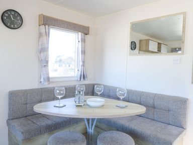 A dining nook with a wooden table chairs corner bench seating and a window with curtains at 31A Foxburrow Hang in Fritton near Belton Norfolk