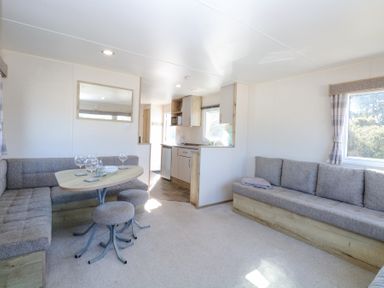 A living area with grey upholstered seating, a wooden table with glassware, and a small kitchen area with cabinets at 31A Foxburrow Hang in Fritton near Belton Norfolk