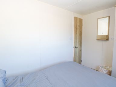 A bedroom with a bed covered in blue bedding a wooden door a mirror on the wall and a basket at 31A Foxburrow Hang in Fritton near Belton Norfolk