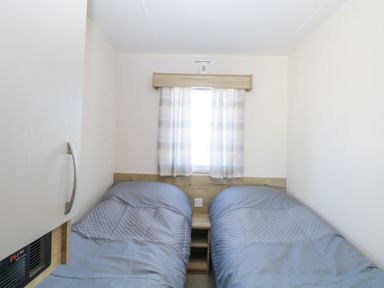 A bedroom with two single beds and a small window with curtains at 31A Foxburrow Hang in Fritton near Belton Norfolk