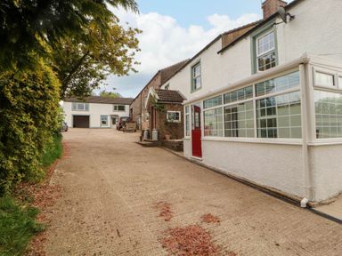 A driveway leading to a white house with a red door and a glass conservatory at Kirkland Howe Cottage in Arlecdon