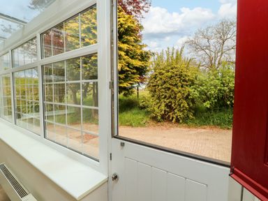 A partially open white door leading to a garden with bushes and trees at Kirkland Howe Cottage in Arlecdon
