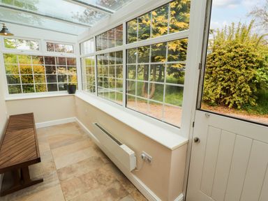 A conservatory with a wooden bench a black plant pot and a heater at Kirkland Howe Cottage in Arlecdon