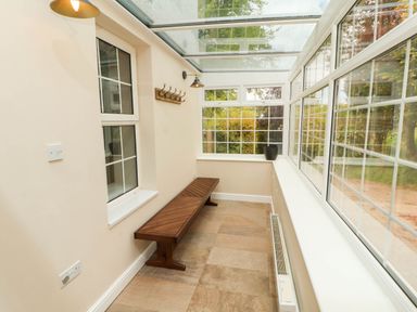 A narrow sunroom with large windows a wooden bench a black plant pot and a wall-mounted coat rack at Kirkland Howe Cottage in Arlecdon
