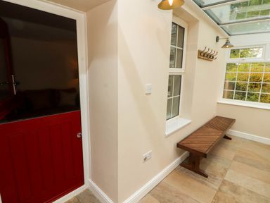 A hallway with a wooden bench a window and a red door at Kirkland Howe Cottage in Arlecdon