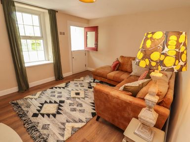 A sitting room with a brown sectional sofa patterned rug and patterned lampshade at Kirkland Howe Cottage in Arlecdon