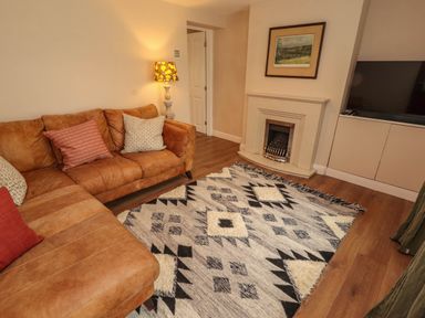 A living room with a brown sectional sofa a patterned rug a fireplace a floor lamp and a television at Kirkland Howe Cottage in Arlecdon