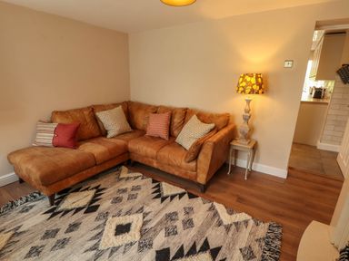 A living room with a brown sectional sofa cushions a wooden side table with a lamp and a patterned rug on the floor at Kirkland Howe Cottage in Arlecdon