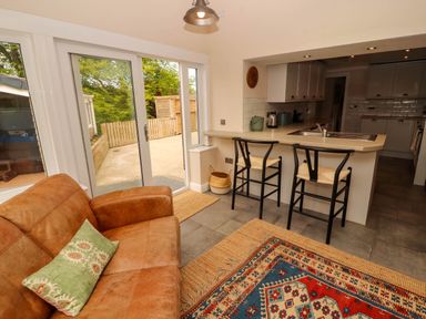 A kitchen area with a counter and two chairs next to a brown sofa and colorful rug at Kirkland Howe Cottage in Arlecdon