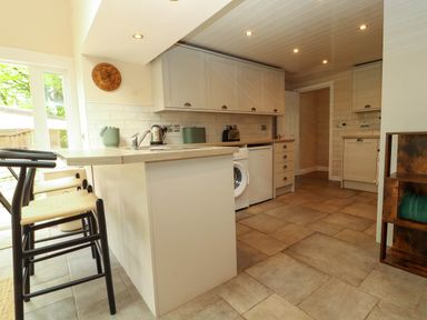 A kitchen with bar stools a washing machine and cabinets at Kirkland Howe Cottage in Arlecdon