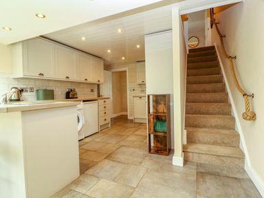 A kitchen with cabinets appliances and tiled floor next to carpeted stairs with a rope handrail at Kirkland Howe Cottage in Arlecdon