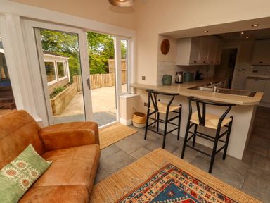 A kitchen with two bar stools at a counter brown sofa and sliding glass doors leading outside at Kirkland Howe Cottage in Arlecdon