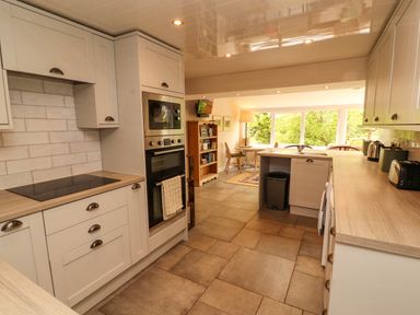 A kitchen with built in oven microwave cooktop and cabinets and a dining area with table chairs and bookshelf at Kirkland Howe Cottage in Arlecdon