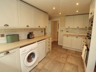 A kitchen with white cabinets a washing machine a mini fridge a toaster and a bread bin at Kirkland Howe Cottage in Arlecdon