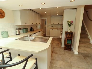 A kitchen with a sink on the island and bar stools next to stairs at Kirkland Howe Cottage in Arlecdon