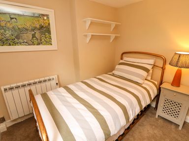 A bedroom with a single bed striped bedding bedside table with lamp wall art and two white shelves at Kirkland Howe Cottage in Arlecdon