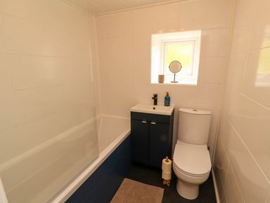 A bathroom with a bathtub a sink cabinet a toilet and a small window at Kirkland Howe Cottage in Arlecdon
