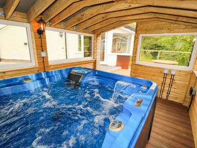 An indoor hot tub with water jets in a wooden room with windows showing an outdoor patio and greenery at Kirkland Howe Cottage in Arlecdon
