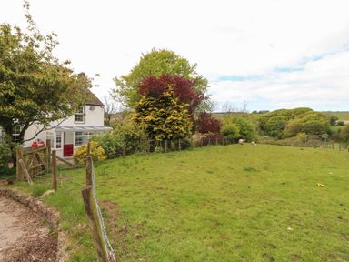 A fenced grassy field with trees and two sheep near a white house with a conservatory at Kirkland Howe Cottage in Arlecdon