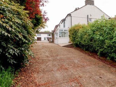 A driveway with hedges on both sides leading to a white house and garage at Kirkland Howe Cottage in Arlecdon