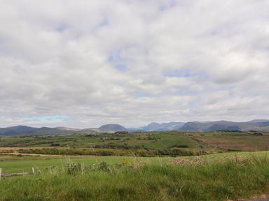 A rural landscape with green fields hills and mountains under a partly cloudy sky at Kirkland Howe Cottage in Arlecdon