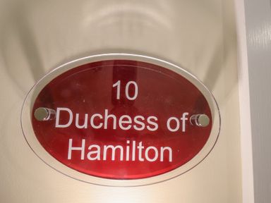 A red oval door plaque with white text reading 10 Duchess of Hamilton