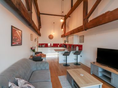 An open living room and kitchen with wooden beams a gray sofa a coffee table and a television at Duchess of Hamilton @ Engine Shed Whitby