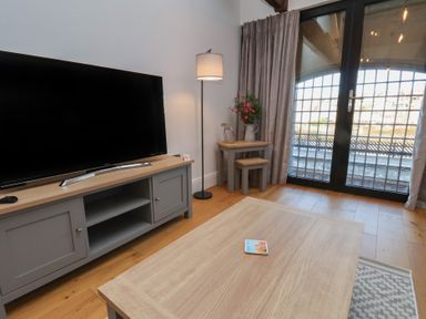A living room with a television on a cabinet a floor lamp and a small table with stools near large glass doors at Duchess of Hamilton @ Engine Shed Whitby