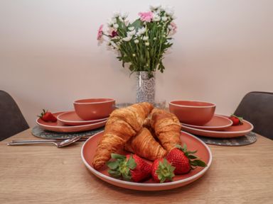 A table set with plates and bowls holding croissants and strawberries with a vase of flowers at Duchess of Hamilton @ Engine Shed in Whitby