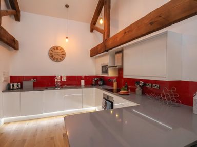 A kitchen with white cabinets gray countertops wooden beams and a red backsplash at Duchess of Hamilton @ Engine Shed in Whitby