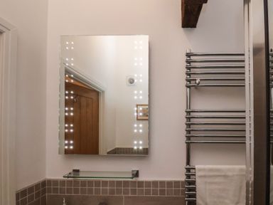 A bathroom mirror with lights around it above a glass shelf and next to a wall-mounted chrome towel heater with a white towel at Duchess of Hamilton @ Engine Shed in Whitby