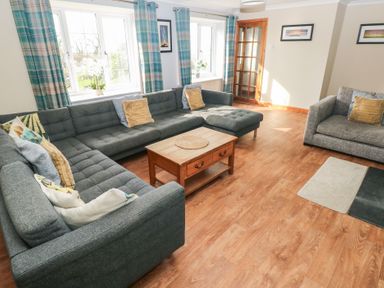 A living room with grey sofas wooden coffee table plaid curtains and framed pictures at Carreg Yr Onnen in Penparc