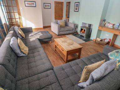 A living room with grey sofas a wood burning stove and a wooden coffee table at Carreg Yr Onnen in Penparc