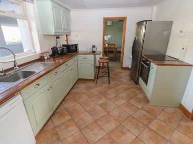 A kitchen with green cabinets brown tiled floor and appliances at Carreg Yr Onnen in Penparc