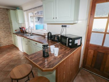 A kitchen with wooden counters stools microwave toaster and kettle at Carreg Yr Onnen in Penparc