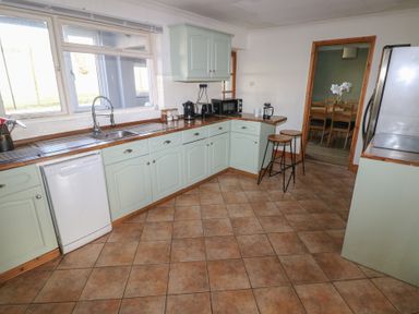 A kitchen with tiled floor wooden countertops light green cabinets and bar stools at Carreg Yr Onnen in Penparc