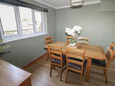 A dining room with a wooden table, six chairs, a white floral centerpiece, window, and green walls at Carreg Yr Onnen in Penparc