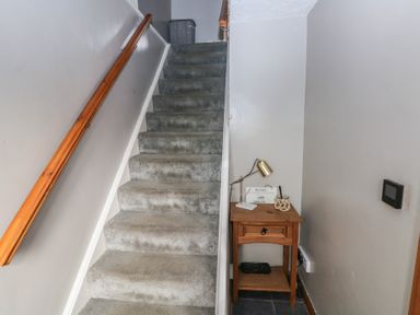 A carpeted staircase with a wooden handrail next to a small wooden table holding a lamp and decorative items at Carreg Yr Onnen in Penparc