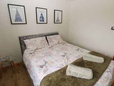 A bedroom with a bed with pillows and bedspread two towels on a blanket and three framed pictures on the wall at Carreg Yr Onnen in Penparc