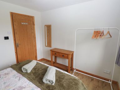 A bedroom corner with a wooden door a small wooden table a mirror and a white clothes rack with hangers at Carreg Yr Onnen in Penparc