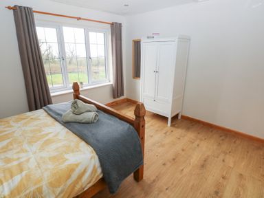 A bedroom with a wooden bed, folded towels on the bed, a white wardrobe, and a window with curtains at Carreg Yr Onnen in Penparc