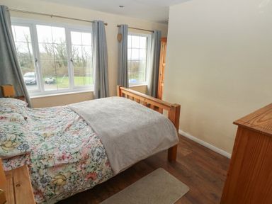A bedroom with wooden bed frame floral bedding and grey curtains at Carreg Yr Onnen in Penparc