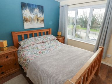 A bedroom with a wooden bed frame and floral bedding two wooden nightstands with lamps and a large window with curtains at Carreg Yr Onnen in Penparc