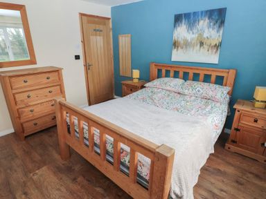 A bedroom with wooden bed frame, chest of drawers, two bedside tables with lamps and a painting on the wall at Carreg Yr Onnen in Penparc