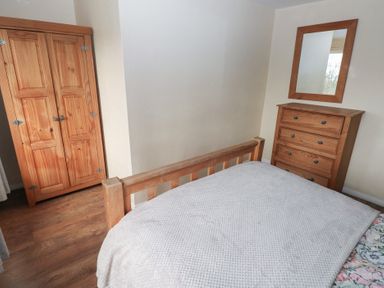 A bedroom with a wooden bed frame wooden wardrobe wooden chest of drawers and a mirror on the wall at Carreg Yr Onnen in Penparc