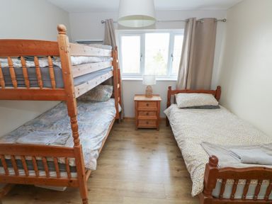 A bedroom with wooden bunk beds a single bed a wooden nightstand and a window with curtains at Carreg Yr Onnen in Penparc
