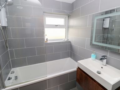 A bathroom with a bathtub shower unit a window a sink with a faucet and a mirror at Carreg Yr Onnen in Penparc