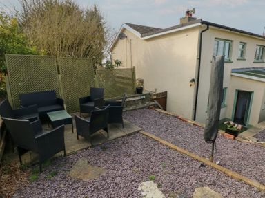 An outdoor patio area with black wicker chairs and a table near a cream building at Carreg Yr Onnen in Penparc