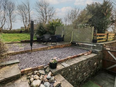 An outdoor patio area with black chairs and a table on a raised platform surrounded by stone walls and a wooden fence at Carreg Yr Onnen in Penparc