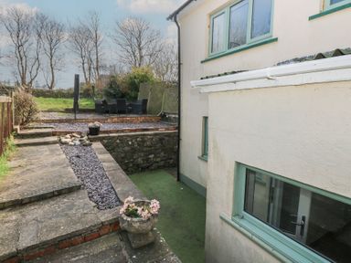 An outdoor patio area with stone steps flower pots seating area and part of a house with green window frames at Carreg Yr Onnen in Penparc
